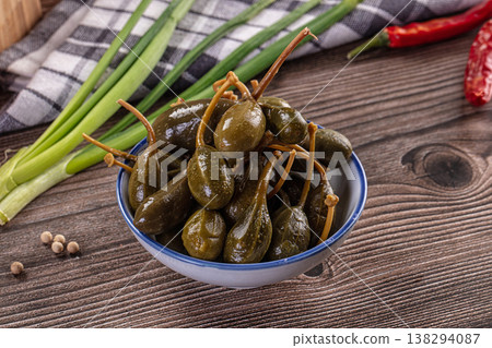 Pickled caper berries in a bowl with fresh ingredients on a rustic wooden table. Pickled caper berries in a bowl with fresh ingredients on a rustic wooden table. 138294087