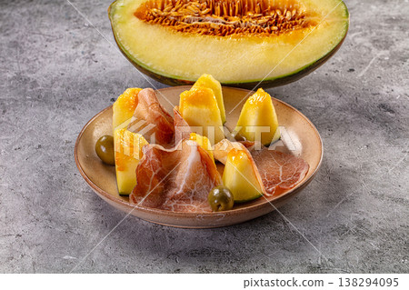 Gourmet appetizer of fresh melon with slices of prosciutto ham and olives on a rustic plate Gourmet appetizer of fresh melon with slices of prosciutto ham and olives on a rustic plate 138294095