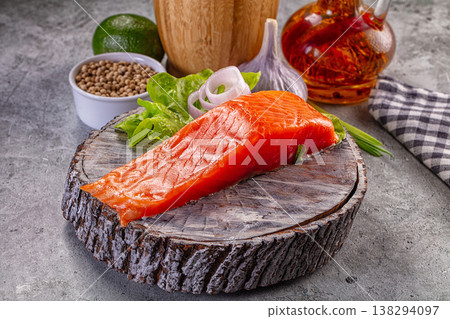Fresh raw salmon fillet on a rustic wooden slice with lime, garlic, coriander, and onion for cooking. Fresh raw salmon fillet on a rustic wooden slice with lime, garlic, coriander, and onion for cooking. 138294097