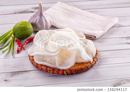 Crispy shrimp chips in a woven basket with fresh chili, lime, and garlic ingredients on a wooden table Crispy shrimp chips in a woven basket with fresh chili, lime, and garlic ingredients on a wooden table 138294117