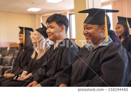 Young people in graduation gowns listen to a speech by a classmate. Young people in graduation gowns listen to a speech by a classmate. 138294488