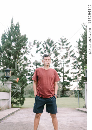 Southeast Asian man standing relaxed with hands in pockets wearing red t-shirt outdoors Southeast Asian man standing relaxed with hands in pockets wearing red t-shirt outdoors 138294542