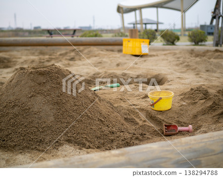 A scene from a park with sandcastles and a yellow bucket, showing signs of sand play. A scene from a park with sandcastles and a yellow bucket, showing signs of sand play. 138294788