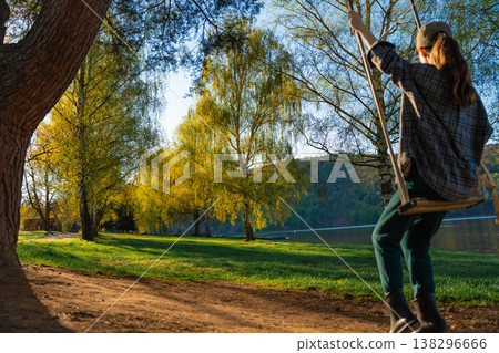 Woman on wooden swing in spring park near lake with copy space and defocused background Woman on wooden swing in spring park near lake with copy space and defocused background 138296666