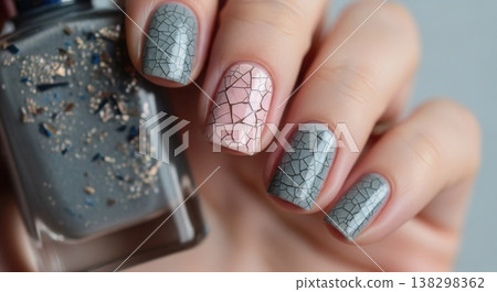 Close-up of a hand holding a bottle of glitter polish, featuring a grey and pink crackle-effect manicure with fine line details. Close-up of a hand holding a bottle of glitter polish, featuring a grey and pink crackle-effect manicure with fine line details. 138298362