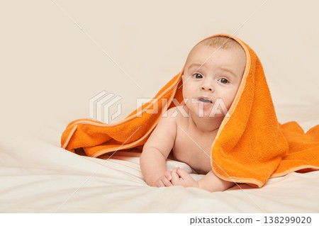 Cute Caucasian Baby With Orange Towel On Head Lying On Bed Smiling Playfully Indoors Portrait Cute Caucasian Baby With Orange Towel On Head Lying On Bed Smiling Playfully Indoors Portrait 138299020