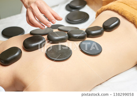 Female Receiving Hot Stone Massage Therapy On Back With Black Basalt Stones For Relaxation Female Receiving Hot Stone Massage Therapy On Back With Black Basalt Stones For Relaxation 138299058