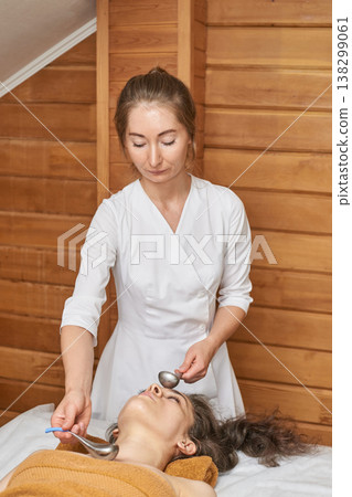 Female Asian Young Adult Giving Relaxing Facial Spa Treatment With Cold Spoons In Wooden Spa Female Asian Young Adult Giving Relaxing Facial Spa Treatment With Cold Spoons In Wooden Spa 138299061