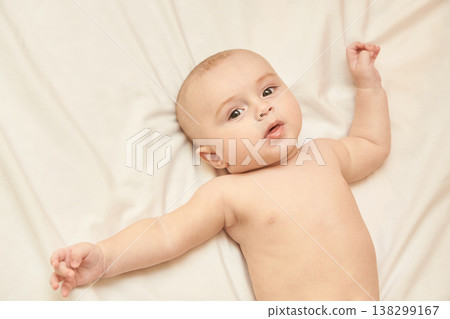 Cute Caucasian Baby Lying On Bed With Outstretched Arms Looking Upward 138299167
