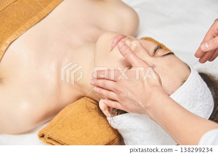 Asian Female Receiving Relaxing Facial Massage At Spa With Towels And Headband, Promoting Skincare Asian Female Receiving Relaxing Facial Massage At Spa With Towels And Headband, Promoting Skincare 138299234