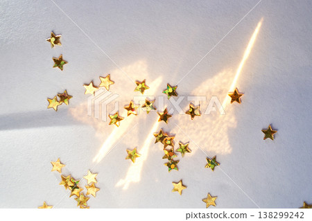 Golden Star Confetti Scattered On White Surface With Sunlight Reflection And Shadows Golden Star Confetti Scattered On White Surface With Sunlight Reflection And Shadows 138299242