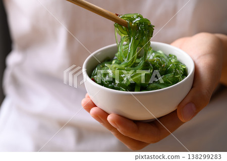 Fresh Japanese seaweed salad (Chuka Wakame) being picked up with chopsticks from a bowl in hand Fresh Japanese seaweed salad (Chuka Wakame) being picked up with chopsticks from a bowl in hand 138299283