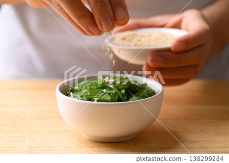 Hand sprinkling white sesame seeds over Japanese seaweed salad (Chuka Wakame) in a bowl Hand sprinkling white sesame seeds over Japanese seaweed salad (Chuka Wakame) in a bowl 138299284