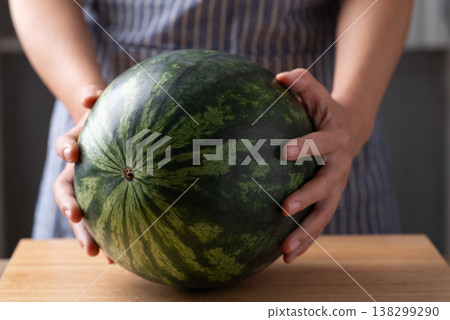Woman's hands placing a fresh watermelon on a wooden cutting board, Tropical fruit in summer season 138299290