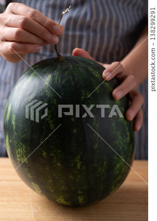 Woman's hands placing a fresh watermelon on a wooden cutting board, Tropical fruit in summer season 138299291