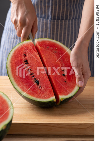 Woman's hands holding a kitchen knife to cut a fresh watermelon on a wooden cutting board Woman's hands holding a kitchen knife to cut a fresh watermelon on a wooden cutting board 138299294