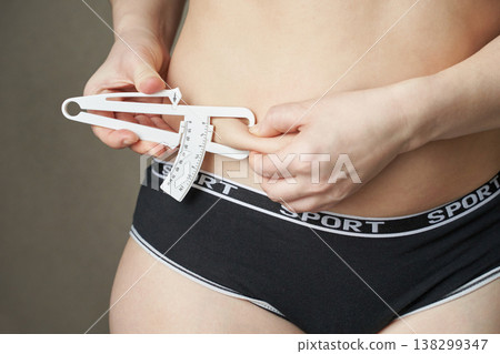 Young caucasian female measuring body fat with caliper in fitness apparel for health monitoring 138299347