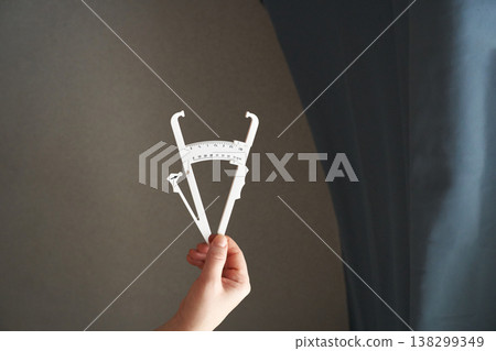 Hand holding calipers indoors against grey and blue background, highlighting precision 138299349