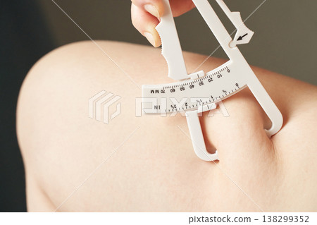 Female hand using skinfold caliper on arm for body fat measurement and fitness assessment 138299352