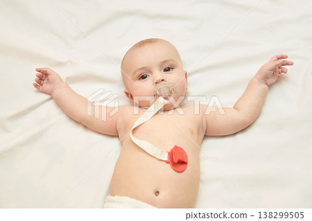 Caucasian Baby Lying On White Bed With Pacifier Relaxing Comfortably With Arms Spread Wide Caucasian Baby Lying On White Bed With Pacifier Relaxing Comfortably With Arms Spread Wide 138299505