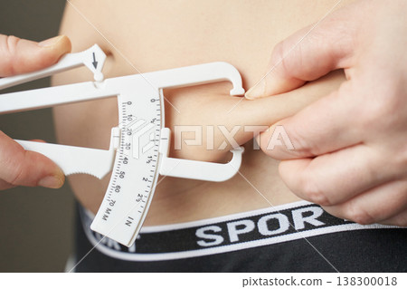 Close-up of body fat measurement with caliper on caucasian male young adult displaying fitness Close-up of body fat measurement with caliper on caucasian male young adult displaying fitness 138300018