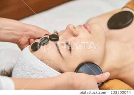 Young Caucasian Female Enjoying Hot Stone Facial Massage At Spa For Relaxation And Wellness Young Caucasian Female Enjoying Hot Stone Facial Massage At Spa For Relaxation And Wellness 138300044