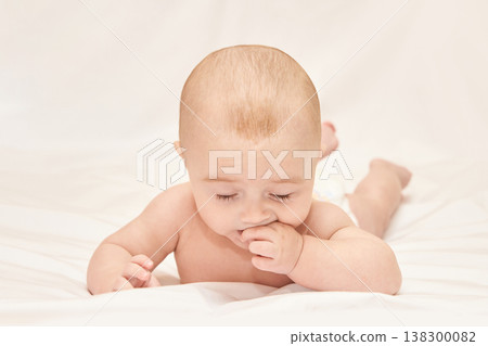 Caucasian Baby Lying On Stomach With Hand In Mouth On White Blanket Caucasian Baby Lying On Stomach With Hand In Mouth On White Blanket 138300082