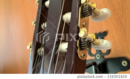 Guitar headstock string tuning peg instrument music acoustic closeup detail classical guitar headstock with metal tuning peg detail and plastic button against wooden background, calm focus 138301829