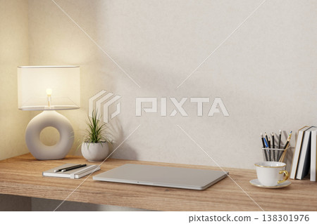 Closed laptop with book and pencil aside hollow lamp and potted plant on wooden table at room corner 138301976