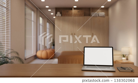 White screen laptop and book on wooden table across wardrobe, pumpkin stool, window blind in bedroom 138302068