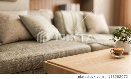 Coffee in glass cup aside potted plant on wooden table aside grey fabric sofa in modern living room. 138302072