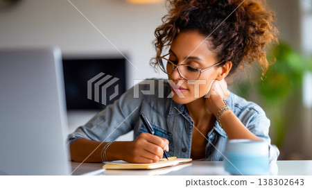 Focused woman writes ideas at desk; woman drafts notes beside laptop, woman adjusts glasses and thinks in bright home office, calm plants and soft light support planning flow, remote work vibe 138302643