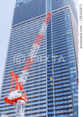 一座正在興建中的高層建築和一台紅白相間的塔式起重機。 一座正在興建中的高層建築和一台紅白相間的塔式起重機。 138302671