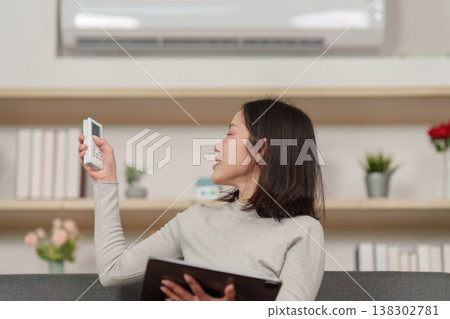 Woman adjusting air conditioner with remote control 138302781