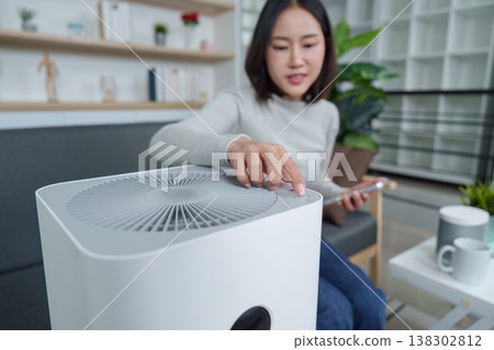 Woman adjusting air purifier settings in modern living room Woman adjusting air purifier settings in modern living room 138302812