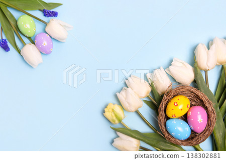 Easter colored painted eggs in bird nest with white tulips on blue background with space for text and greetings. Easter and spring concept. Spring background 138302881