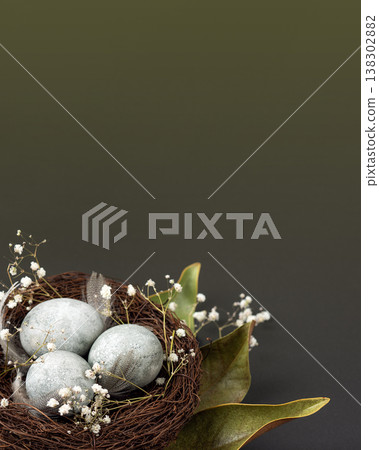Brown nest of twigs with three gray Easter eggs, feathers, dried magnolia leaves and sprigs of gypsophila on black green gradient background. Minimalistic Easter concept 138302882