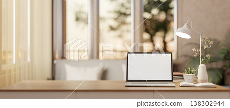 White screen laptop with book and coffee aside lamp on wooden table across window in the living room 138302944