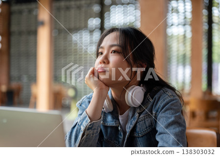 Bored asian woman resting head on a hand looking over laptop while sitting waiting at table in cafe. Bored asian woman resting head on a hand looking over laptop while sitting waiting at table in cafe. 138303032