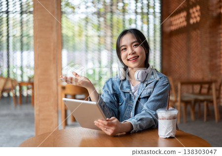 Pretty asian woman holding tablet and open palm aside coffee on wooden table while sitting in cafe. Pretty asian woman holding tablet and open palm aside coffee on wooden table while sitting in cafe. 138303047
