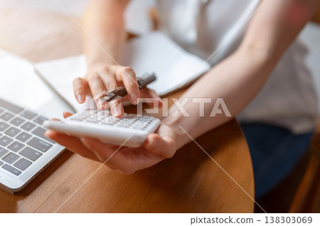 Close up of a woman's hands holding pen using calculator over laptop while sitting at table in cafe. 138303069