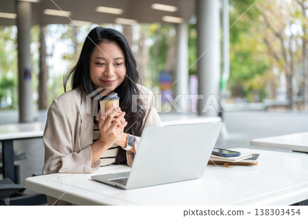 Happy asian woman hands holding coffee looking at laptop as sitting at table in university building. Happy asian woman hands holding coffee looking at laptop as sitting at table in university building. 138303454
