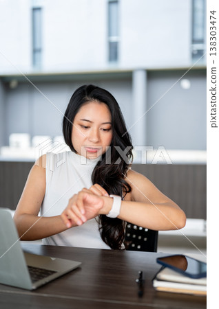 Smart asian woman looking at watch checking time aside laptop while sitting at wooden table in cafe. Smart asian woman looking at watch checking time aside laptop while sitting at wooden table in cafe. 138303474