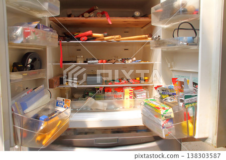 A broken refrigerator is being used as a storage unit for tools and other items. A broken refrigerator is being used as a storage unit for tools and other items. 138303587
