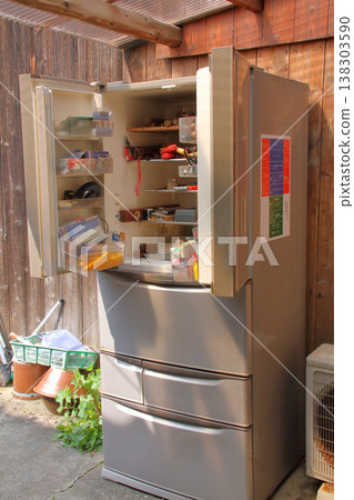 A broken refrigerator is being used as a storage unit for tools and other items. 138303590