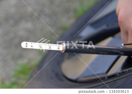 This image shows someone checking tire pressure using a pencil-type air gauge when changing to summer tires. 138303613