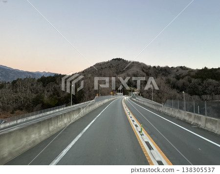 黃昏時分,一條公路蜿蜒穿過山區,朝著行進方向彎曲。 黃昏時分,一條公路蜿蜒穿過山區,朝著行進方向彎曲。 138305537