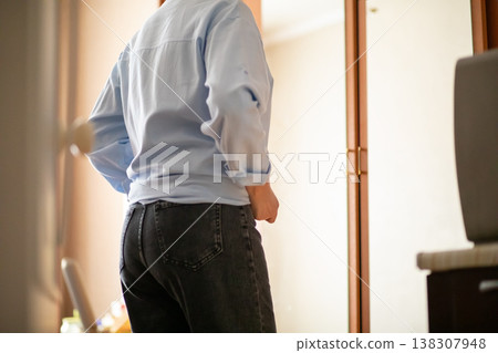 Middle aged woman in light blue shirt and dark jeans looking at her reflection in home mirror. Mature lady checking her appearance. Concept of self care and fashion styling at home. 138307948