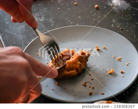Man cutting crispy fried chicken with fork and knife on plate. Close up view of delicious fast food meal. Preparation of tasty breaded poultry dish for eating at home dinner table. Man cutting crispy fried chicken with fork and knife on plate. Close up view of delicious fast food meal. Preparation of tasty breaded poultry dish for eating at home dinner table. 138308167