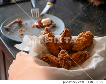 Man eating deep-fried chicken wings from a paper basket. Crispy appetizer served at home. Casual meal, hungry person enjoying fast food snack. Delicious culinary experience and diet concept. 138308172